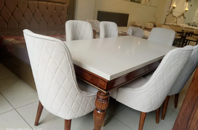 A white dining table with tufted white chairs and a wooden base